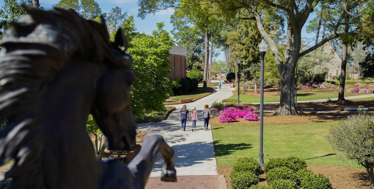 students walking on campus with stallion in foreground